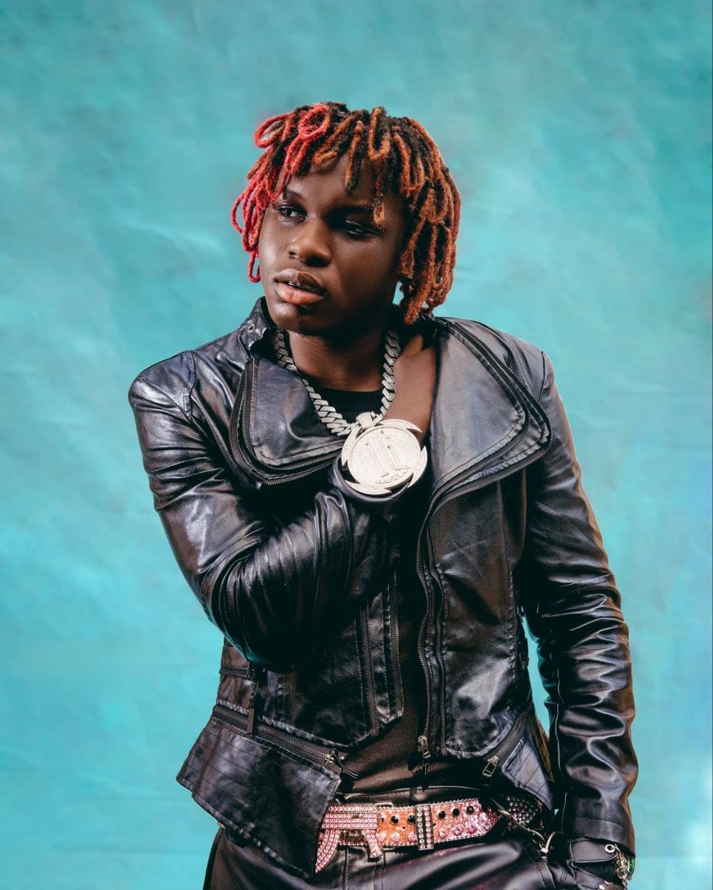 Ayo Maff in a black leather jacket against a teal backdrop